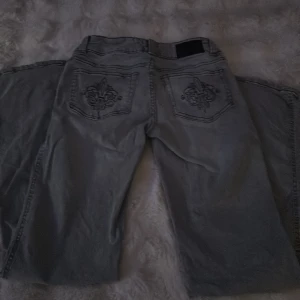 Grå jeans med broderade bakfickor 157 - Snygga grå jeans från 157 med broderade detaljer på bakfickorna. Klassisk femficksmodell med raka ben och normal passform. Jeansen har en cool, lite tvättad look och är perfekta för dig som gillar stilrena men ändå unika detaljer.