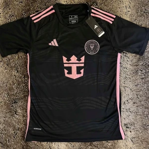 Inter Miami fotbollströja - Svart Inter Miami fotbollströja från Adidas i storlek S med rosa detaljer och klubbmärke på bröstet. Tröjan är i väldigt skönt matrial och inte använd, Så strålande skick. Pris kan diskuteras vid snabb affär🤭 så tveka inte vid intresse! Frågor om Bilder och Passform. Är bara kontakta mig🤩🤝