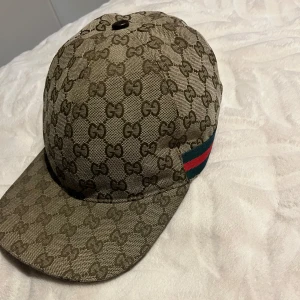Gucci GG Supreme keps beige M - Exklusiv Gucci keps i beige GG Supreme-mönster med klassiska gröna och röda ränder på sidan. Kepsen har böjd skärm och justerbar rem bak. Tillverkad i canvas med ikoniskt monogramtryck och levereras med originalbox och dustbag. Pris kan diskuteras och hör av er för frågor.