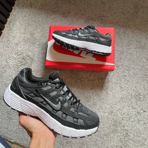 Nike P-6000 black and grey  - Nike P-6000 sneakers i svart och grått med vit, chunky sula. Ovandel i mesh och syntet med coola detaljer och snörning. Perfekta för dig som gillar sportig och trendig stil. Swoosh-logga på sidan och Nike-märke på plösen.