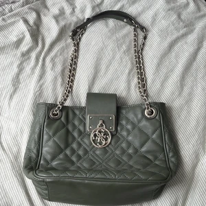 Grön quiltad axelväska från Guess - Snygg grön axelväska från Guess i quiltat skinn med silverfärgade kedjehandtag och logga framtill. Väskan har ett coolt leopardmönstrat innerfoder och dragkedja på insidan. Perfekt för dig som vill ha en trendig och praktisk väska med lyxig känsla, självklart äkta💕