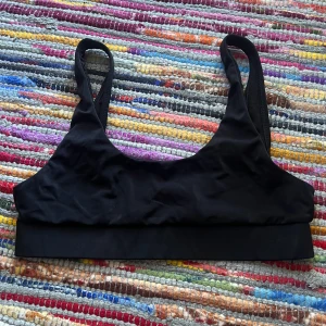 Nelly Bikini överdel  - En stilren svart bikini överdel från Nelly med bred resår under bysten och klassiska axelband. Snygg, enkel design utan mönster och med en tight passform som sitter på plats. Materialet känns mjukt och stretchigt. M, men passar s 