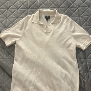 Vit pikétröja från H&M, regular fit - Klassisk vit pikétröja från H&M i regular fit. Tröjan har korta ärmar, mjuk krage och v-ringad öppning utan knappar. Perfekt basic-plagg i bomull som funkar till många olika stilar.