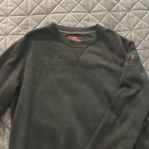 Svart fleece-tröja från Parajumpers - Mysig svart fleece-tröja från Parajumpers med rund halsringning och diskret logopatch på ärmen. Tröjan har ribbade muddar och är perfekt för kyliga dagar. Enkel och stilren design som funkar till det mesta.