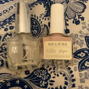 Nagellack Maybelline & NailKind - Två nagellack: Maybelline Express Finish 40 i genomskinlig färg med silvrigt lock och NailKind Vegan i en ljusrosa nyans med vitt lock. Båda i fyrkantiga glasflaskor, perfekt för snygga naglar och enkel applicering.