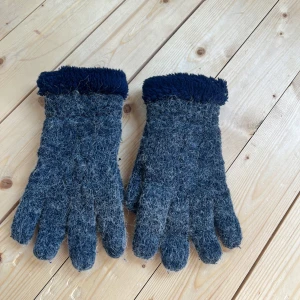 Mörkgrå ullhandskar med blå fleecefoder - Säljer ett par riktigt mysiga mörkgrå stickade ullhandskar med fluffigt mörkblått fleecefoder vid handleden. Perfekta för kalla dagar när du vill hålla händerna varma och sköna. Klassisk modell med fem fingrar och grovstickad känsla.