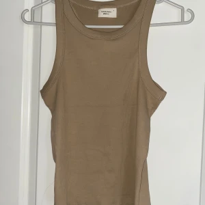 Beige ribbad linnetopp från Gina Tricot - Säljer en stilren beige ribbad linnetopp från Gina Tricot. Toppen är ärmlös med rund halsringning och har en tight passform. 