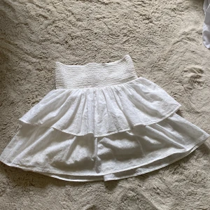 Vit volangkjol från KappAhl - Superfin vit kortkjol från KappAhl med broderade små blommor och dubbla volanger. Kjolen har bred smock i midjan för skön passform och är gjord i bomull. Perfekt för sommarens alla tillfällen! Jättefin kjol som passar bra till de mesta! 