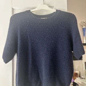 Mörkblå stickad tröja från Chelsea - Mysig mörkblå stickad tröja från Chelsea med korta ärmar och rund halsringning.  I lama päls där av väldigt mjuk. Tröjan kan bara handtvättas ny pris 400kr. 