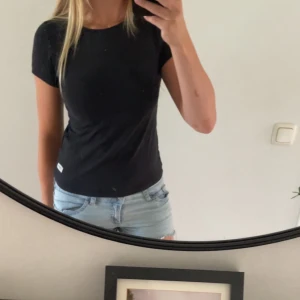 Svart basic t-shirt - En svart, enkel och stilren t-shirt med korta ärmar och rund hals. Modellen är figurnära och passar perfekt till jeans eller shorts. T-shirten är i mjuk bomull och har en liten vit etikett nertill på sidan.