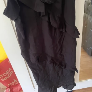 Svart långklänning med volangdetaljer - Svart klänning med snygga volangdetaljer längs hela klänningen. Ärmlös modell med axelband och flowy .  Materialet känns lätt och passar bra till varmare dagar. Aldrig använd