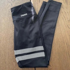 Svarta träningstights från Stronger - Svarta träningstights från Stronger. Fint skick men finns ett hål vid ett av benen. Men det ska inte vara några problem att laga. Hög midja.