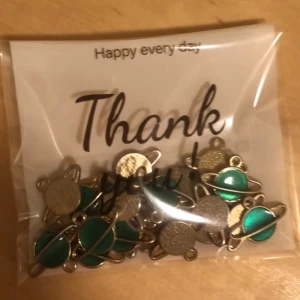 Pack med Gröna planet-berlocker i metall - Säljer ett pack med 20 st små berlocker i form av guldiga planeter med grönfärgade detaljer. Perfekta att använda till armband, halsband eller örhängen. Berlockerna har en cool rymd-look och är tillverkade i metall med grön emalj. 