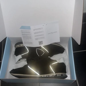  Philippe Model skor - Säljer ett par snygga svarta sneakers från Philippe Model med vita detaljer och reflekterande inslag. Skorna har snörning och en unik sula med kamouflagemönster. Längst fram på sulan har släppt på båda skorna som syns på bild 4. Det finns också en defekt inuti vid hälen på båda skorna. Obs endast skorna, Philippe model lapp och boxen ingår. 