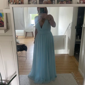 Ljusblå balklänning med v-ringning - Säljer en superfin ljusblå balklänning från JJ’s House med djup v-ringning, slits och smala axelband som korsas i ryggen. Klänningen har ett flowigt fall och markerad midja. Använd 1 gång, st 42 men är något minde i storleken, så den är som en st 40