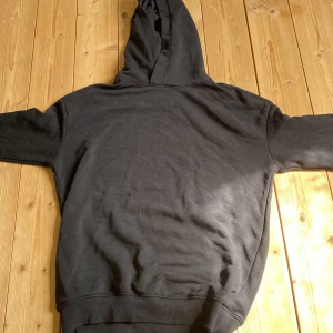 Svart hoodie från H&M med huva - En klassisk svart hoodie från H&M i storlek 146. Tröjan har en skön huva, långa ärmar och ribbade muddar vid ärmslut och nederkant. Perfekt för en chill och avslappnad stil. Materialet är mjukt och bekvämt, troligtvis bomullsmix.