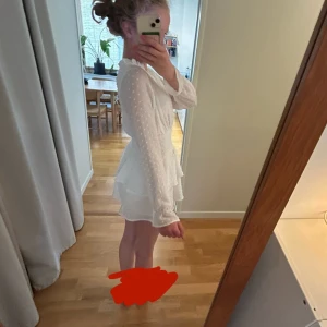 Vit kort volangklänning med lång ärm - Supersöt vit kortklänning med volanger och långärmade, lätt transparenta ärmar. Klänningen har v-ringning, smock i midjan och ett diskret prickigt mönster i tyget. Perfekt för sommarens alla tillfällen! Är liten på mig som är 164cm. Kontakta mig vid funderingar ❤️