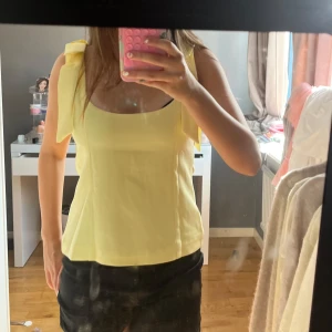 Gul linnetopp med knytband - Supersöt ljusgul linnetopp med breda axelband som knyts till rosetter. Toppen har en rak, något figurnära passform och fyrkantig ringning. Perfekt för till alla outfits! Endast testad 