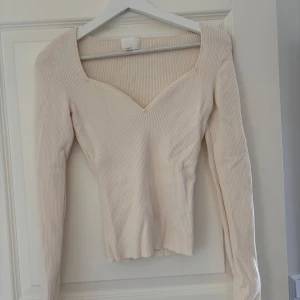 Ribbad beige långärmad tröja H&M - Superfin ribbad långärmad tröja från H&M i en ljus beige nyans. Tröjan har en snygg v-ringad halsringning och figurnära passform. Perfekt att styla med jeans eller kjol för en clean look.