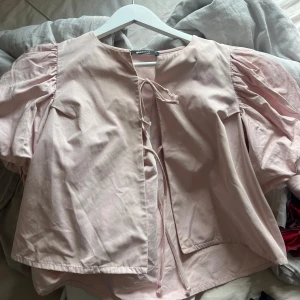 Ljusrosa blus med puffärm Gina Tricot - Supersöt ljusrosa blus från Gina Tricot med puffiga ärmar och knyt framtill. Blusen har en rak passform och är tillverkad i mjuk bomull. Perfekt för dig som gillar romantiska detaljer och en feminin look.