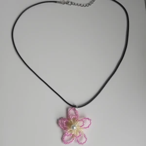 Halsband med pärlblomma  - Supergulligt halsband med en handgjord blomma av små pärlor i rosa och ljusgul, med en vit pärla i mitten. Kedjan är justerbar 