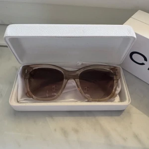 Beige CHIMI solglasögon modell 07 - Snygga solglasögon från CHIMI i modellen 07, färg Ecru. Glasögonen har en transparent beige båge och bruna tonade glas. Kommer i originaletui och box. Perfekt accessoar för soliga dagar och ger en cool vibe till din outfit.