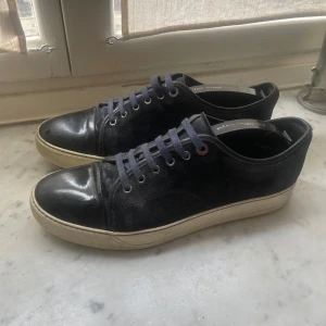 Feta Lanvin Cap Toe sneakers - Snygga mörkblå sneakers från Lanvin med ovandel i mocka och blankt tåparti. Skorna har mörkblå snörning och vit platt sula. De har lackats om och snörena är nästintill sprillans nya. Skorna är för små för mig så säljer av det skälet. Liten defekt som syns på sista bilden. Priset är ej hugget i stenen, så hör av er vid minsta fundering!🙌          Dustbag ingår.