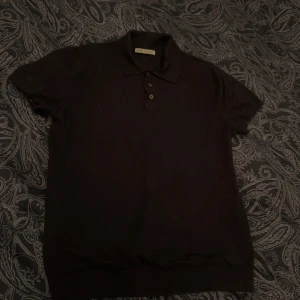 Svart pikétröja från Zara, stl S - Klassisk svart pikétröja från Zara i storlek S. Tröjan har korta ärmar, krage och tre knappar framtill. Perfekt basic-plagg med ribbade muddar i ärmslut och nederkant. Enkel och stilren design som funkar till det mesta.