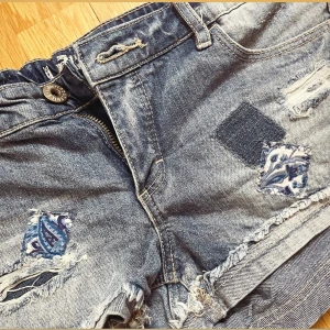 Jeansshorts  - Super fina blå jeansshorts, med låg midja och slitna detaljer samt patchade mönster i blått och vitt. Lappen sitter inte kvar men skulle gissa på XXS / XS🌸 Perfekta för sommaren och festivaler.