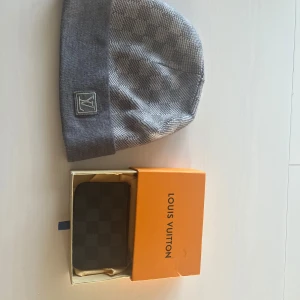 Grå rutig mössa&Grå rutig plånbok - Snygg grå mössa  med klassiskt rutigt mönster och uppvikt kant. Logga framtill i silver på en fyrkantig patch. Mjuk och bekväm, perfekt för kyliga dagar. Stilren design som lyfter vilken outfit som helst. Även en grå plånbok, stilren och bra för att förvara kort osv. 