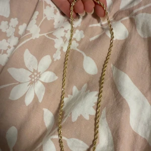 Guldigt halsband från SNÖ of Sweden - Säljer ett snyggt halsband från SNÖ of Sweden i guldton. Kedjan har en tvinnad design som ger ett lyxigt intryck och är försedd med en rund SNÖ-tag vid låset. Perfekt accessoar för att lyfta din outfit. Ungefär 40cm lång guldpläterad.