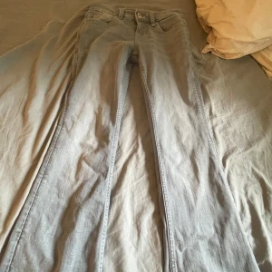 Grå bootcut jeans med broderade fickor - Snygga grå jeans med bootcut passform och coola broderade detaljer på bakfickorna. Klassisk femficksmodell med bälteshällor och dragkedja. Perfekta för dig som gillar en avslappnad men ändå trendig look.