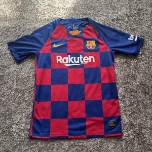 Barcelona match tröja - Säljer en FC Barcelona matchtröja från Nike med klassiskt rutigt mönster i blått och rött. Tröjan har korta ärmar, klubbmärke och sponsorer tryckta på bröstet och ärmen. Tillverkad i lätt och ventilerande material, perfekt för fotbollsplanen.