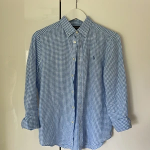 Blårutig skjorta från Polo Ralph Lauren - Snygg blårutig skjorta från Polo Ralph Lauren i storlek L. Skjortan har klassisk krage, långa ärmar och knäppning framtill. Tillverkad i mjuk bomull och har den ikoniska broderade loggan på bröstet. Perfekt för en clean och stilren look.