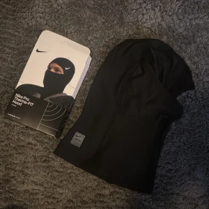 Nike Pro Therma-FIT svart balaclava - Nike Pro Therma-FIT Hood i svart, perfekt för träning utomhus. Tight passform som täcker hela huvudet och halsen. Snyggt Nike Swoosh-tryck på sidan och Nike Pro-märke framtill. Tillverkad i mjukt och stretchigt syntetmaterial för maximal komfort.