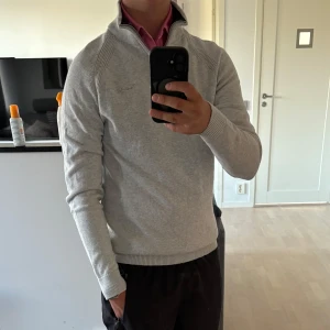 Ljusgrå stickad tröja Bondelid M - Snygg ljusgrå stickad tröja från Bondelid i storlek M. Tröjan har en hög krage med half zip-dragkedja och ribbade muddar vid ärmslut och nederkant. Perfekt för lager-på-lager och chill stil under höst och vinter.