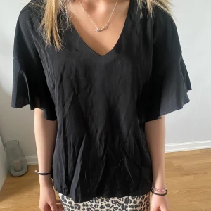 Svart blus med volangärmar - En svart blus med v-ringning och volangärmar. Luftig och skön passform som ger en avslappnad men ändå stilren look.