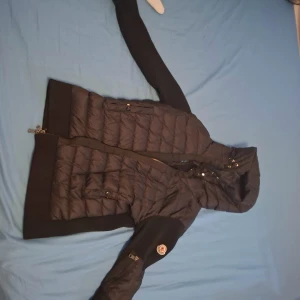 Svart Moncler dunjacka med huva - Säljer en svart Moncler dunjacka med huva och dragkedja. Jackan har quiltad framsida och ärmar med Moncler-logga på ena ärmen. Baksidan och delar av ärmarna är stickade för en snygg kontrast. Perfekt för kyliga dagar och riktigt stilren look. Nypris 14000 kr.