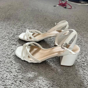 Vita sandaler med klack och knut - Snygga vita sandaler från Clou i storlek 37. De har fyrkantig tå, bred klack och remmar med knutdetalj framtill samt justerbar ankelrem. Nypris 450, Endast använda 2 gånger✨