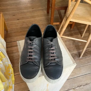 Gråa sneakers från Axel Arigato - Stilrena svarta sneakers från Axel Arigato i mjukt skinn med bruna snören och vit sula. Klassisk låg modell med rund tå och diskret guldfärgad logga på sidan. Perfekta för dig som gillar minimalistisk och clean stil.