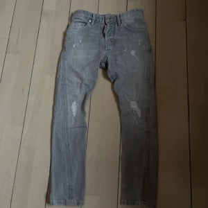 Grå slitna jeans från dsq2 - Grå jeans från dsq2 med slitningar och små färgstänk för en cool, avslappnad look. Klassisk femficksmodell med raka ben och knappgylf. Perfekta för dig som gillar streetstyle och vill ha ett par jeans med attityd. 146-152