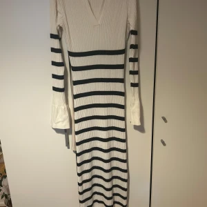 Vit och svart ribbad långklänning NA-KD - Långärmad ribbad långklänning i vitt med svarta horisontella ränder. Klänningen har v-ringning och utsvängda ärmslut för en cool touch. Figurnära passform och stretchigt material som känns bekvämt och trendigt.