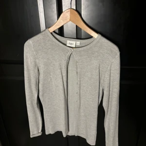 Ljusgrå kofta från Saint - Ljusgrå kofta från Saint i mjuk bomull med rund halsringning och knappar framtill. Enkel och stilren design med långärmad passform, perfekt att slänga på sig över en t-shirt eller linne.