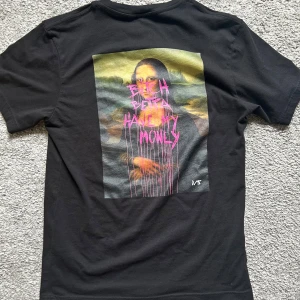 Svart t-shirt med tryck XS - Svart t-shirt i bomull med korta ärmar. På ryggen finns ett stort färgglatt tryck med text i rosa och gult, och framtill står det 'NEVER BROKE AGAIN' i vitt. Skön passform och perfekt för dig som gillar streetwear vibes.