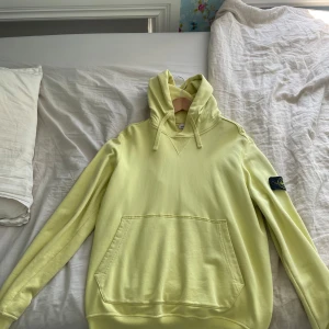 Gul hoodie från Stone Island - Snygg ljusgul hoodie från Stone Island med klassisk patch på ärmen. Två små hål i ryggen som ni ser på bild, köpt från NK