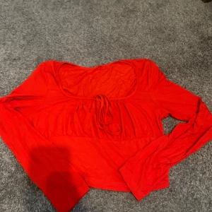 Två långärmade croppade toppar röd - Säljer två snygga långärmade croppade toppar i rött och vinrött. Den ena har knytning framtill och djup urringning, den andra har twistad detalj vid bysten. Båda är i mjuk bomullskänsla och passar perfekt till jeans eller kjol.