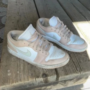Nike Air Jordan 1 Low beige/vit 38.5 - Nike Air Jordan 1 Low sneakers i beige och vitt med klassisk swoosh på sidan. Lågt skaft, snörning och perforerad tåbox. Skorna har en stilren och clean look med mjuka färgtoner och ikonisk Jordan-logga på hälen. Perfekta för dig som gillar streetstyle.