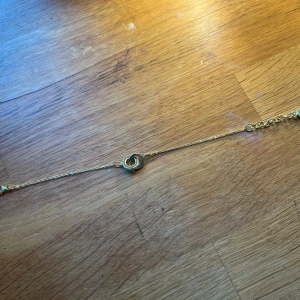 Guldigt armband från Snö of Sweden - Snyggt armband i guldton från Snö of Sweden med tunn kedja och två sammanlänkade ringar som detalj. Armbandet har en liten rund bricka med Snö-loggan vid låset. Perfekt accessoar för att lyfta din stil. Helt nytt aldrig använt! PRIS KAN DISKUTERAS