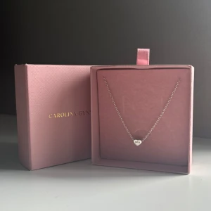 Halsband Carolina Gynning  - Silver halsband från Carolina Gynning med ett hjärta med texten 'you' ingraverat. Hjärtat har stenar runt om dig. Kommer i original ask. Nästintill aldrig använd. Nypris:890kr