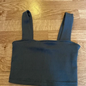 Ribbad grå linnetopp från H&M Divided - Snygg ribbad grå linnetopp från H&M Divided i storlek XS. Toppen har breda axelband och croppad passform, perfekt till jeans eller kjol. Enkel och stilren design som är lätt att matcha med andra plagg.